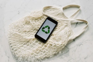 A smartphone with a recycle symbol on top of a bag laid on a table.